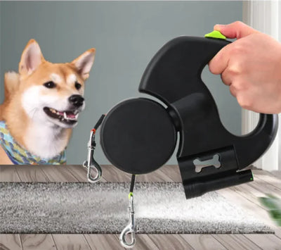 Black retractable dog leash with a hand holding it, next to a dog on a mat.